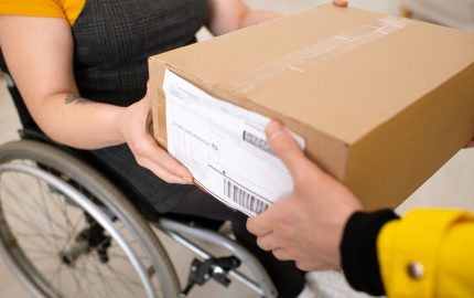 Close-up of deliveryman giving package to customer in wheelchair