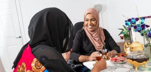 Two ladies in head scarves sharing tea together. One of them has a spinal cord injury and uses a wheelchair.